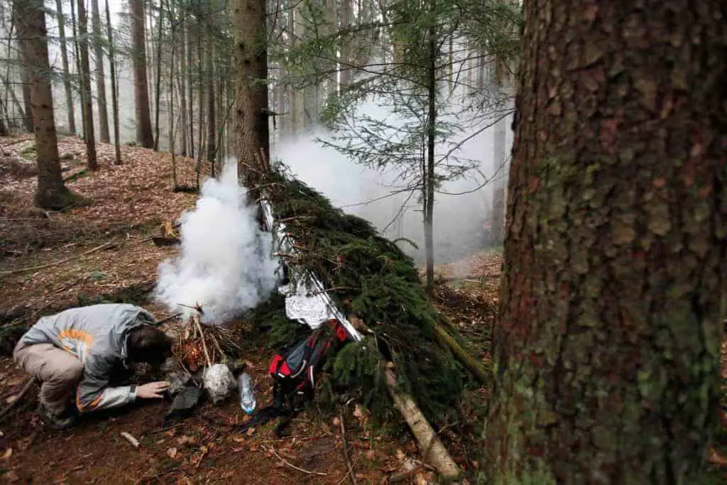 Man starting a fire near his survival lean to shelter